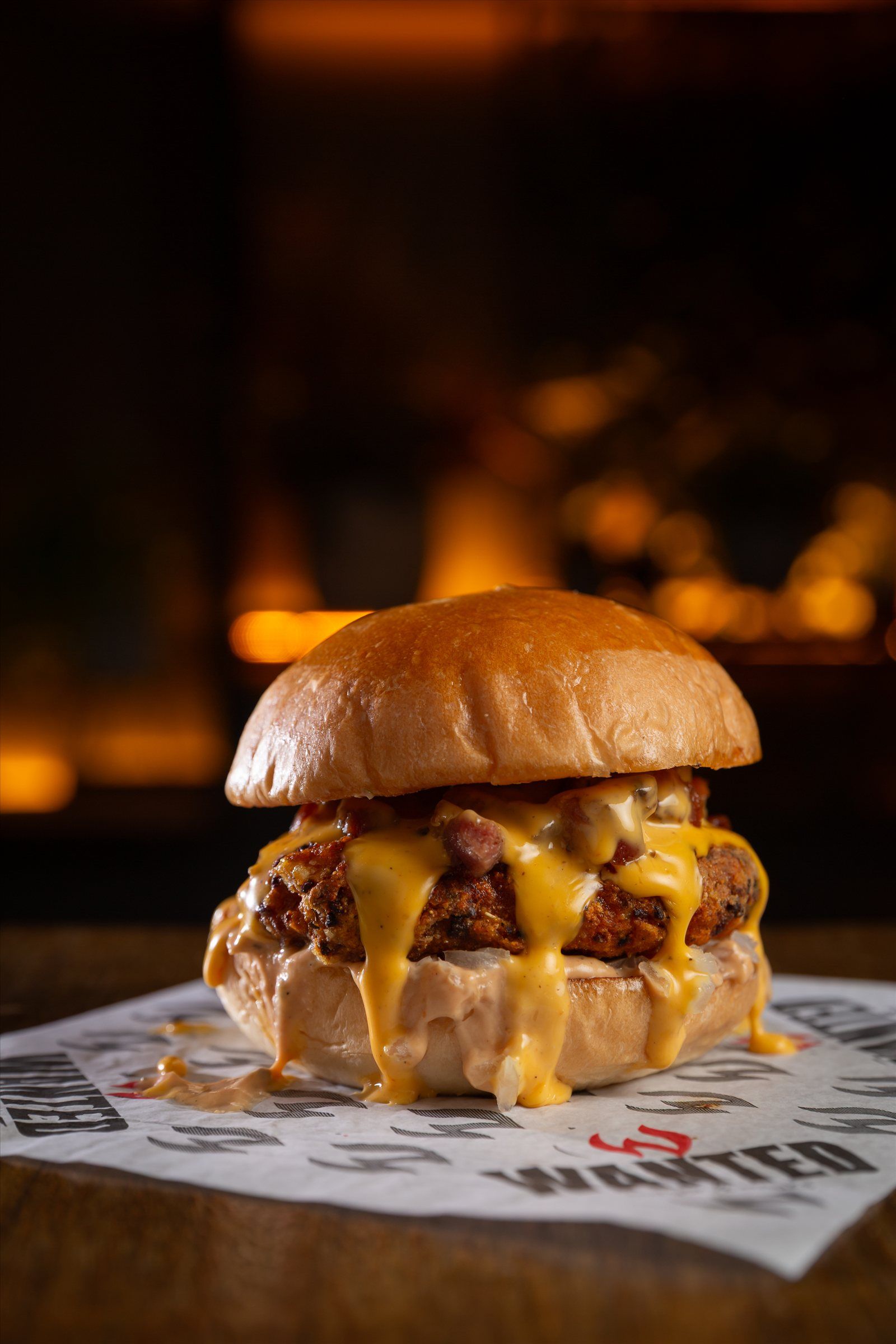 Burger com cheddar derretido sobre o papel da Wanted, luzes âmbar do salão ao fundo
