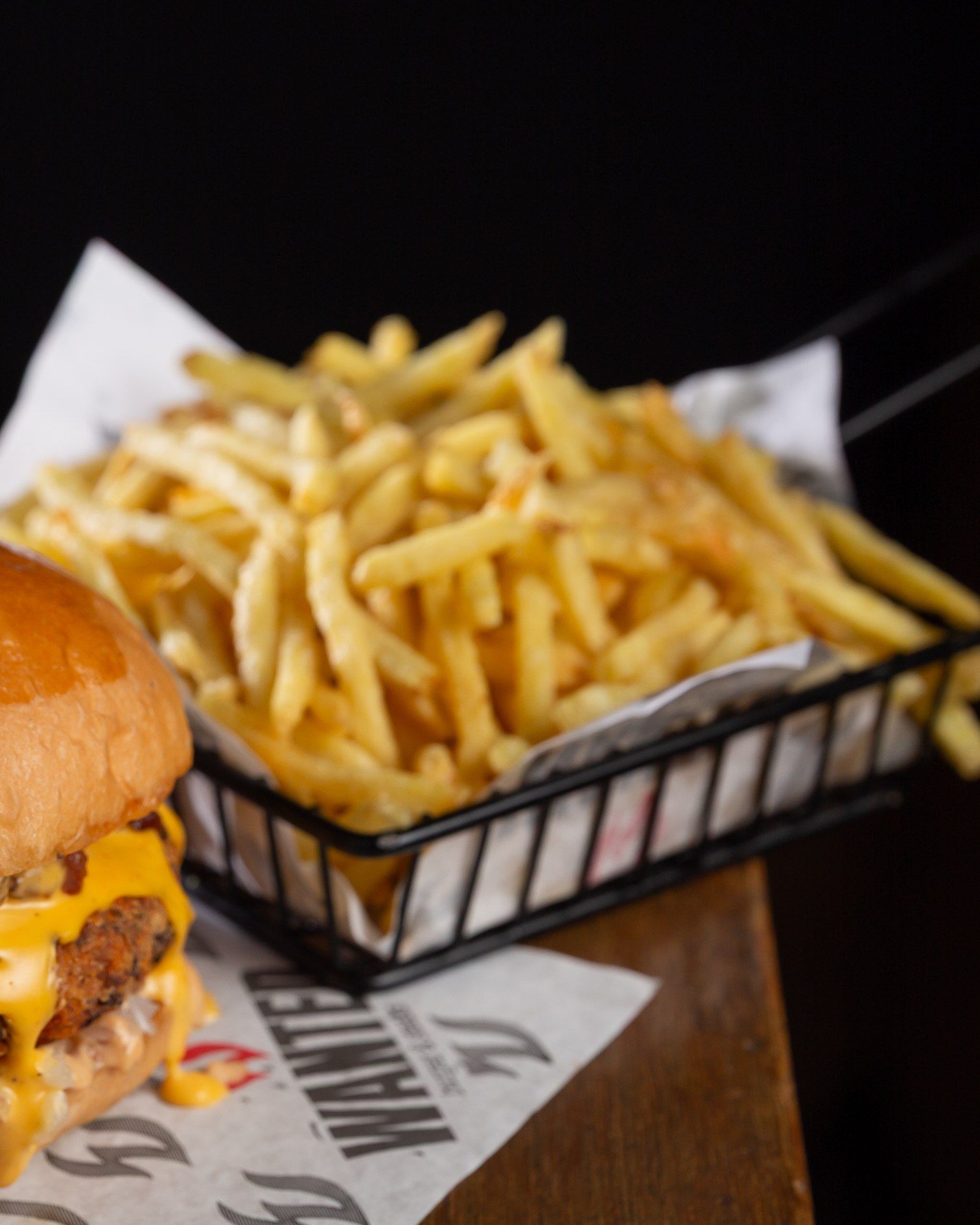 Batata da Vovó: batata fininha e dourada na cestinha forrada com o papel da Wanted, ao lado de um burger com cheddar