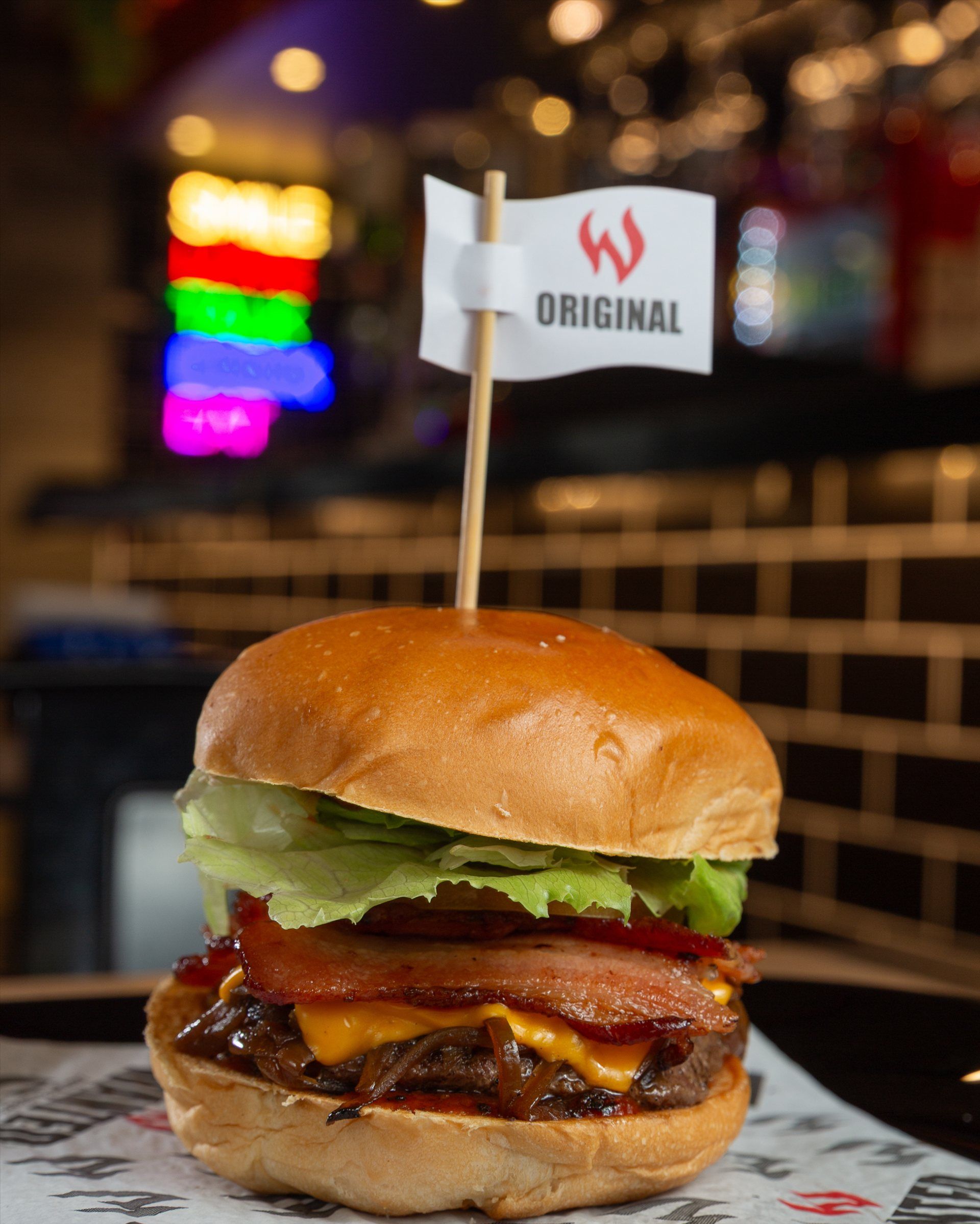 Burger Original com a bandeirinha da Wanted, neon colorido do salão ao fundo